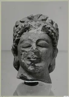Limestone head sculpture from Kition with closed eyes, curled hair and a worn nose and chin