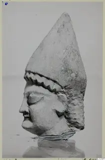 Limestone head statue from Kition in profile, with a tall pointed headdress and a zigzag ridged band across the brow.