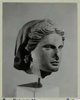 Marble head of a woman with wavy hair swept back under a veil, shown on a square stand.