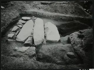 Excavation at Amathus with three large pale stone slabs standing in a trench, surrounded by smaller stones.