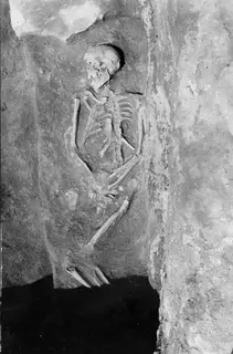 Skeleton lying in Tomb 16 at Amathus, with the skull, ribcage and arm bones visible against the tomb wall.