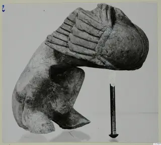 Limestone sculpture fragment from Vouni with a ribbed upper section, photographed beside an iron nail