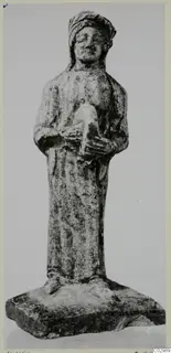 Limestone figurine from Vouni of a standing robed figure with a head covering, holding a small object at the chest