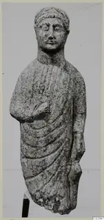 Limestone statue from Vouni of a standing figure in a draped cloak, one arm bent across the chest.