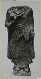 Headless limestone statue of a standing figure in a long draped garment, on a rough base, from Vouni