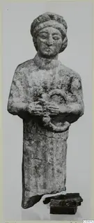 Small limestone standing figure from Vouni, arms folded across the chest and hands holding a ring-shaped object.