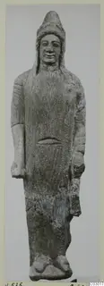 Limestone statue of a standing figure in a long garment and tall cap, photographed against a grey backdrop.