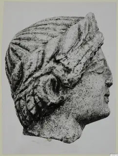Carved limestone head in profile facing right, with grooved hair and a curled lock beside the ear.
