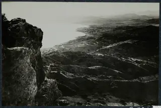 View from a rocky outcrop over a bay and rolling hills near Vouni, with scattered trees and a track winding across the slopes