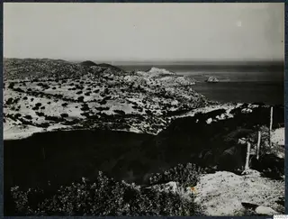 Rocky, scrubby hillside falling to the sea at Vouni, with a small offshore rock.
