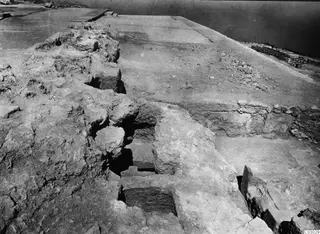 Excavated walls and rubble at the palace at Vouni, with a low stone wall and the sea beyond