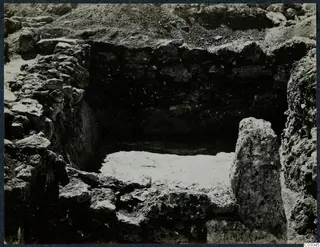 Excavated stone-walled pit at Vouni Palace with a standing stone block on the right and a pale floor surface.