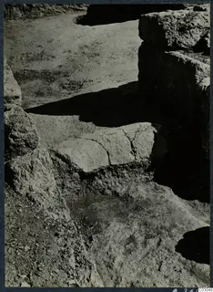 Excavated area at Vouni palace with rough stone blocks, a cracked flat slab, and a standing wall in shadow