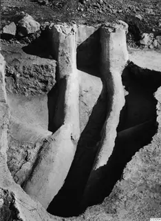 Excavation trench at Vouni palace with two tall plastered wall stubs rising from the cut, with loose stones on the ground above