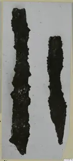 Two corroded iron tools lying side by side, one tapering to a point, on a pale background