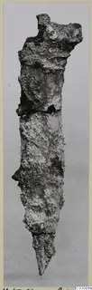 Corroded iron dagger blade, photographed upright against a grey backdrop.