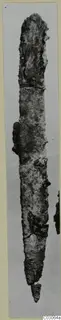 Long corroded iron knife, photographed upright, with a small fragment broken off near its tip.