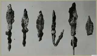 Row of corroded iron arrowheads with long tangs, photographed against a plain grey background.