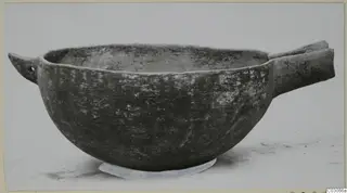 Black Slip Ware bowl with two horizontal handles, photographed from the side on a pale background.