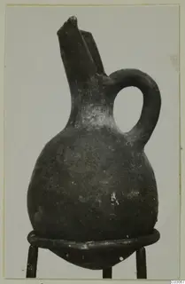 Black-slipped jug with a tall trefoil-type spout and a loop handle, standing on a metal stand