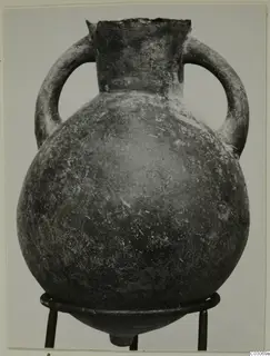 Black-slipped pottery amphora with two loop handles and a wide round body, photographed on a metal stand.