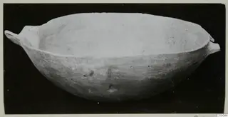 Plain white hand-made bowl with two small handles, photographed against a black background