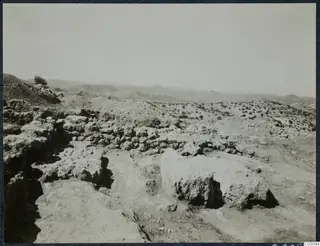 Rocky ground with stone walls and foundations in the foreground, scrubby trees and hills at Vouni