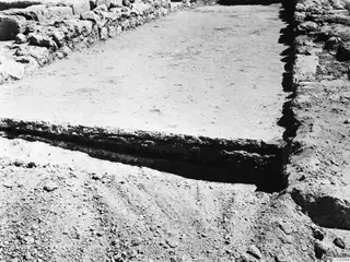 Excavated area at Vouni with a stone wall along its edges and a trench cut along the near side of a flat, pale surface