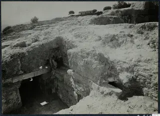 Excavated stone blocks and wall faces at Vouni palace, with a small stone building and trees on the ridge behind