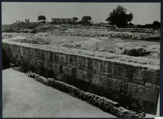 Long wall of large dressed stone blocks at the palace at Vouni, with people and a small building behind