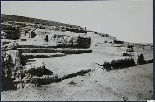 Stone walls and stepped stone ledges at Vouni Palace, with two people standing on the ridge above.