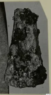 Heavily corroded iron tool with a tapering shape, shown on a grey card.