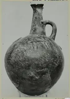 Red Polished I vessel from Lapithos with a tall narrow neck and a single loop handle, shown on a clear stand