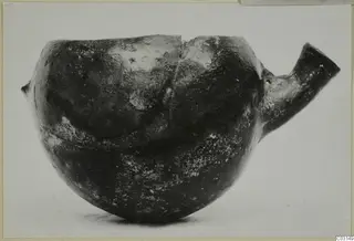 Dark glossy pottery vessel with a tubular spout to the right and a small lug on the left.