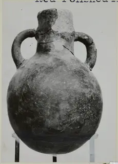 Red Polished III amphora from Lapithos with two loop handles and a broken neck, against a pale background