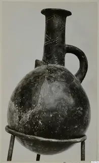 Red Polished III jug from Lapithos, with a single handle and incised neck decoration, shown on a metal stand