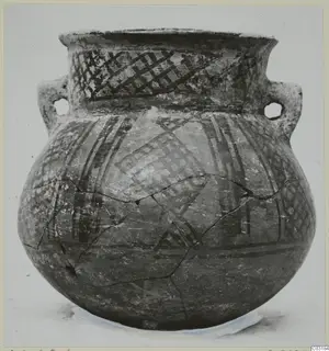 Round-bodied pottery jar with two handles and painted criss-cross and band decoration, shown on a stand against a plain background.