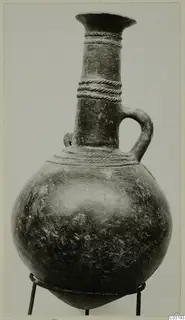 Globular jug with a tall neck, flaring rim, twisted raised bands and a single loop handle, standing on a metal stand.