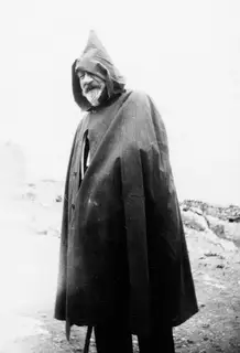 G. Jeffery standing in a hooded dark cape on stony open ground at Vouni.
