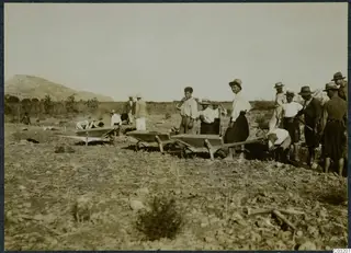 Workers with wheelbarrows in a stony field at Soli, with a rounded hill on the left