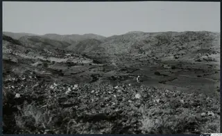 Hilly landscape at Soli with scattered pale stones in the foreground and one standing person in the middle distance
