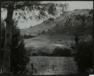 Mountain landscape at Ayios Iakovos with a pine tree in the foreground, a rocky hill, spoil heaps and a small group of people