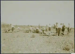 Workers with wheelbarrows and shovels in a stony, open field at Soli.