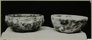 Two cast glass bowls on a white cloth against a black background, one with a ribbed outer wall and a cracked rim