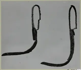 Two corroded bronze toilet implements with looped tops and curved, pointed ends, photographed side by side.