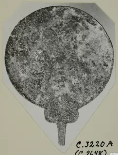 Round, heavily corroded metal plate with a narrow tang projecting from its base, from Marion.