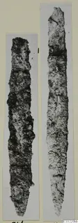 Two corroded metal blades, narrow and tapering, photographed side by side on pale mounts.