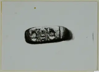 Dark oblong object with three engraved panels, possibly a ring bezel or seal