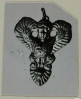 Pendant with a loop at the top, a central face between two round openings, and flaring side lobes with ridged surfaces