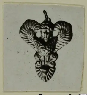 Ornamental pendant with a loop at the top, a small face at the centre and fan-shaped flaps, from Marion Tomb 60